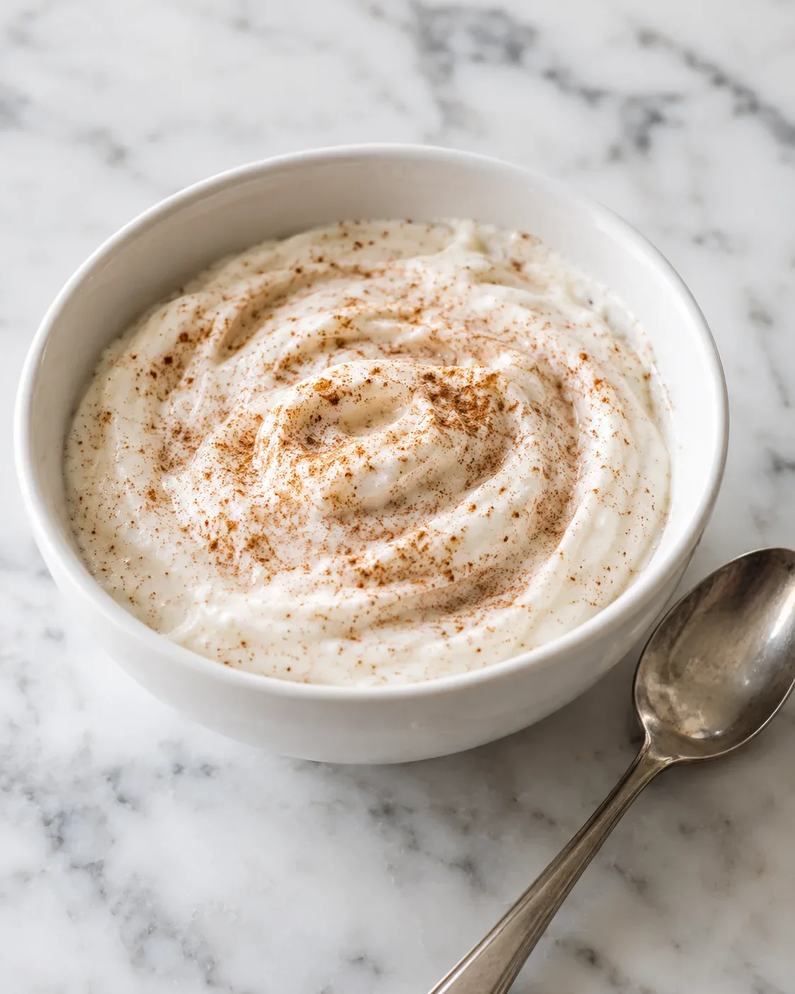 Vanilla Greek yogurt stirred with ground cinnamon in a small bowl before being divided into snack-box cups.