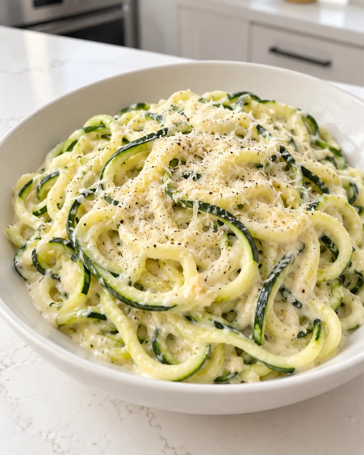 Creamy cottage cheese Alfredo sauce tossed with zucchini noodles and Parmesan in a white bowl.
