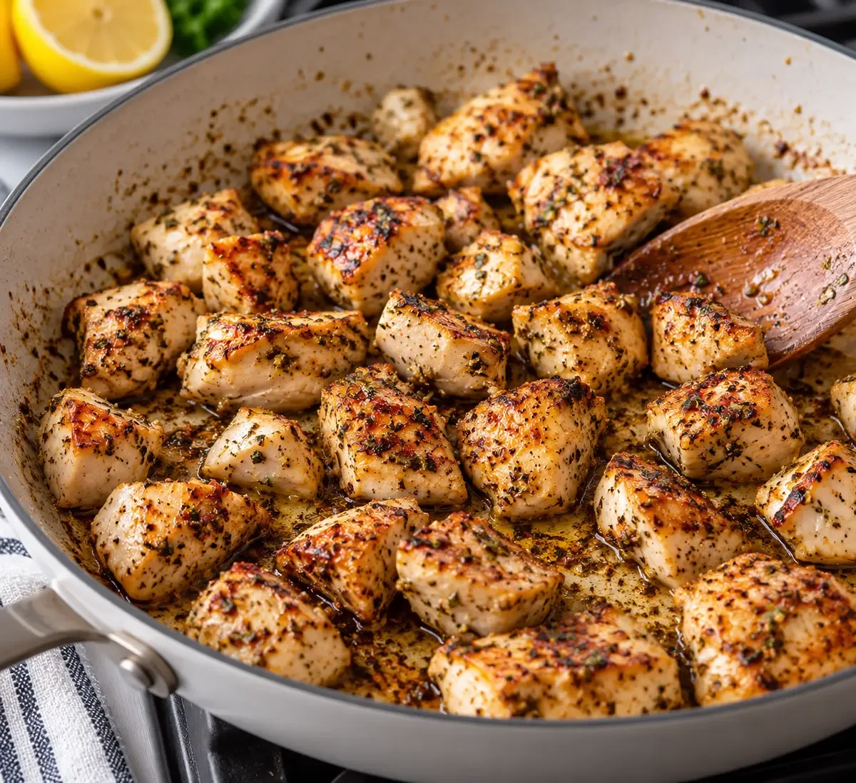 Seasoned chicken breast pieces browning in a skillet with a wooden spoon.