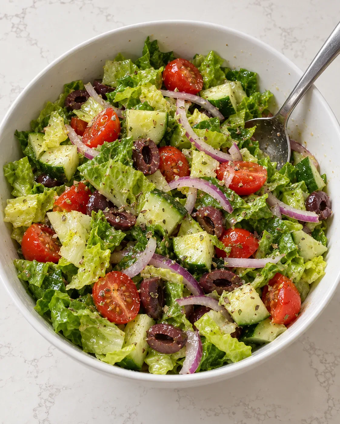 Romaine, tomato, cucumber, red onion, and sliced Kalamata olives lightly dressed in a white bowl