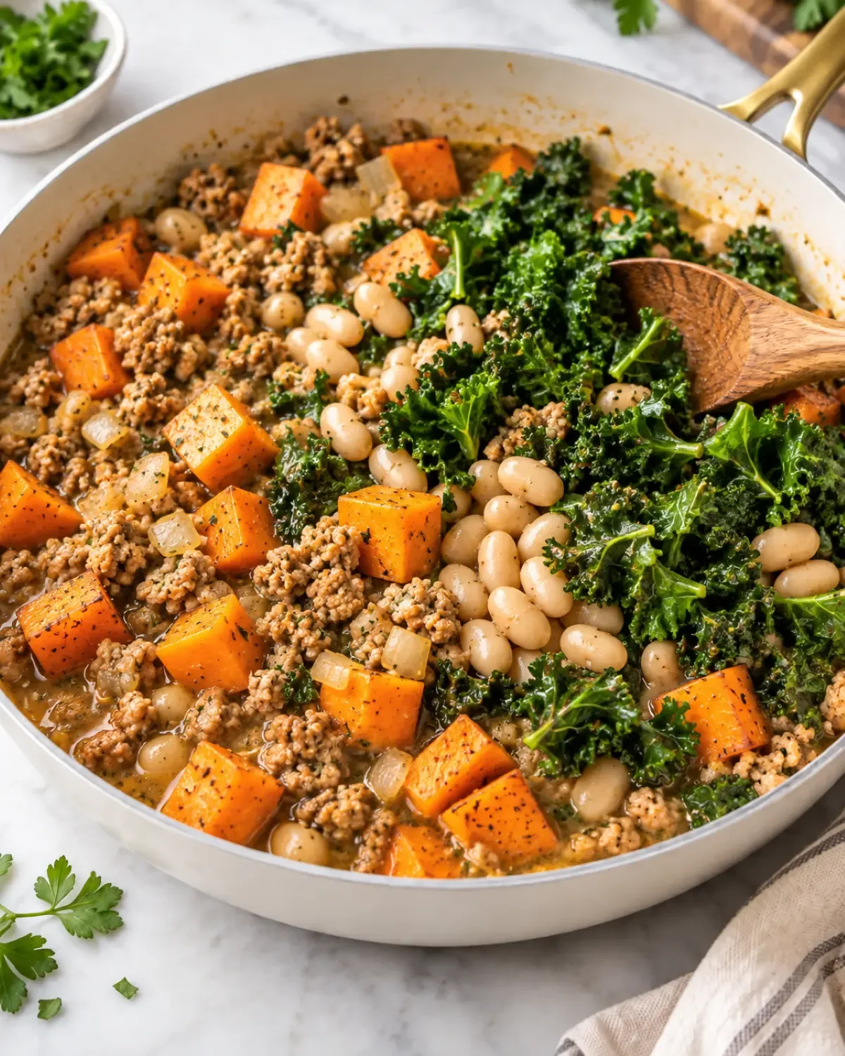 Ground turkey, sweet potatoes, white beans, and kale cooking in a skillet