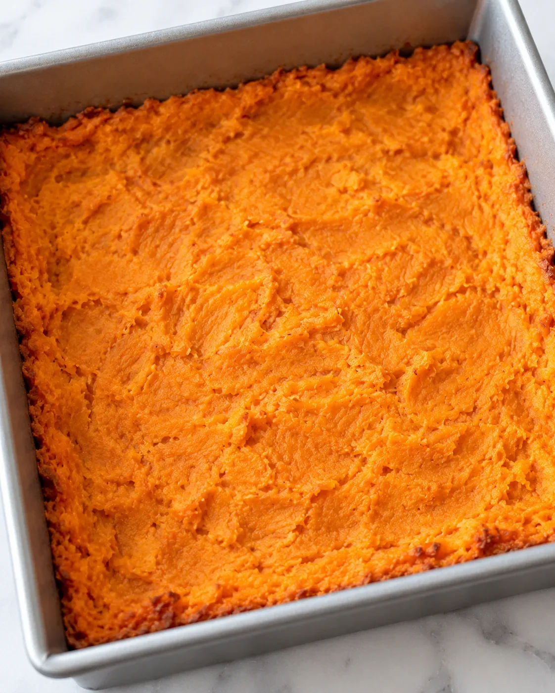 Pressed, lightly browned mashed sweet potato crust in an eight-inch square metal baking pan before egg filling is added.