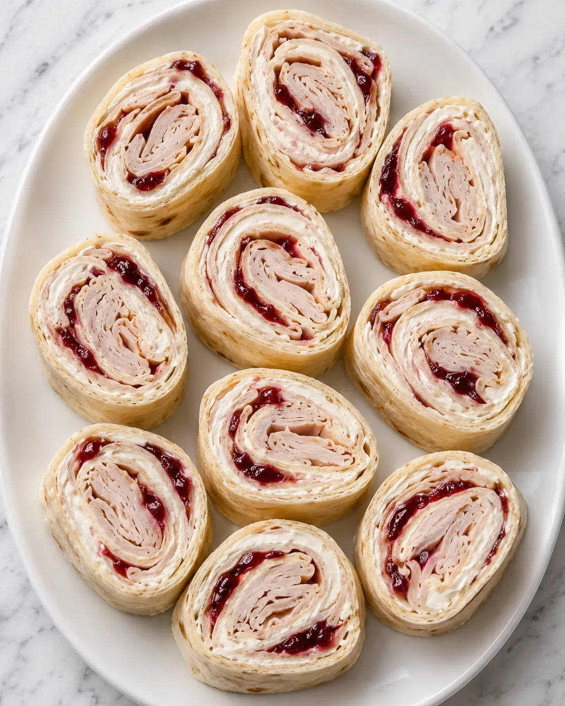 Turkey, cream cheese, and cranberry tortilla pinwheels on a white platter.