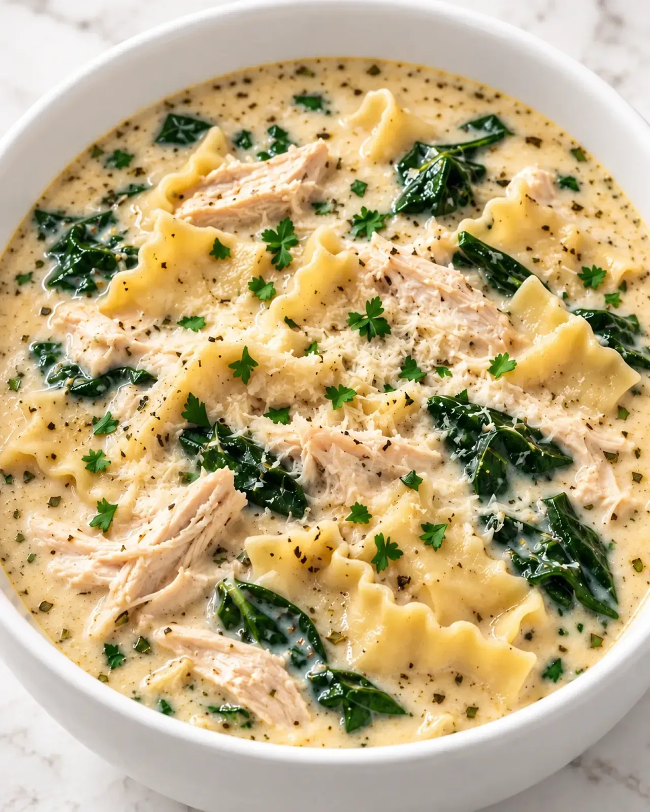 White chicken lasagna soup with shredded chicken, spinach, and broken lasagna noodles in a creamy cottage cheese broth.